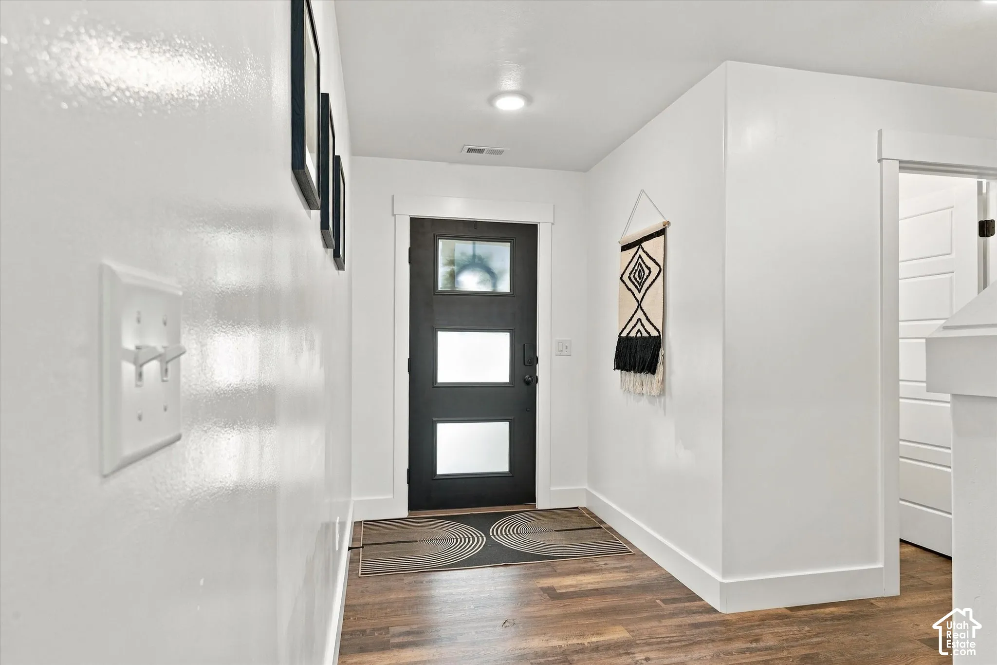 Wood-finish flooring, white walls, and a black front door with frosted glass panels