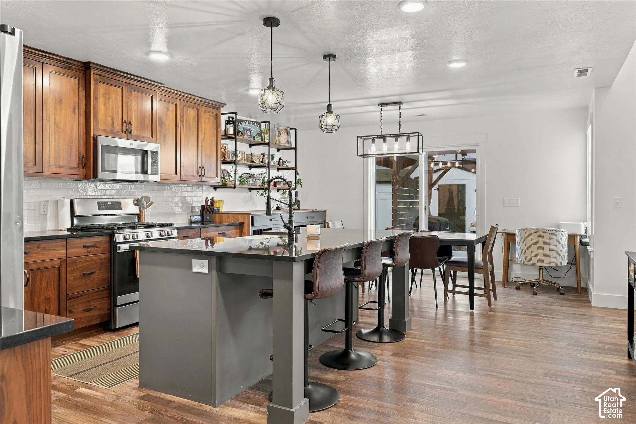 Kitchen featuring wood-finish cabinetry, stainless steel appliances, a large center island with seating, a tile backsplash, and recessed lighting