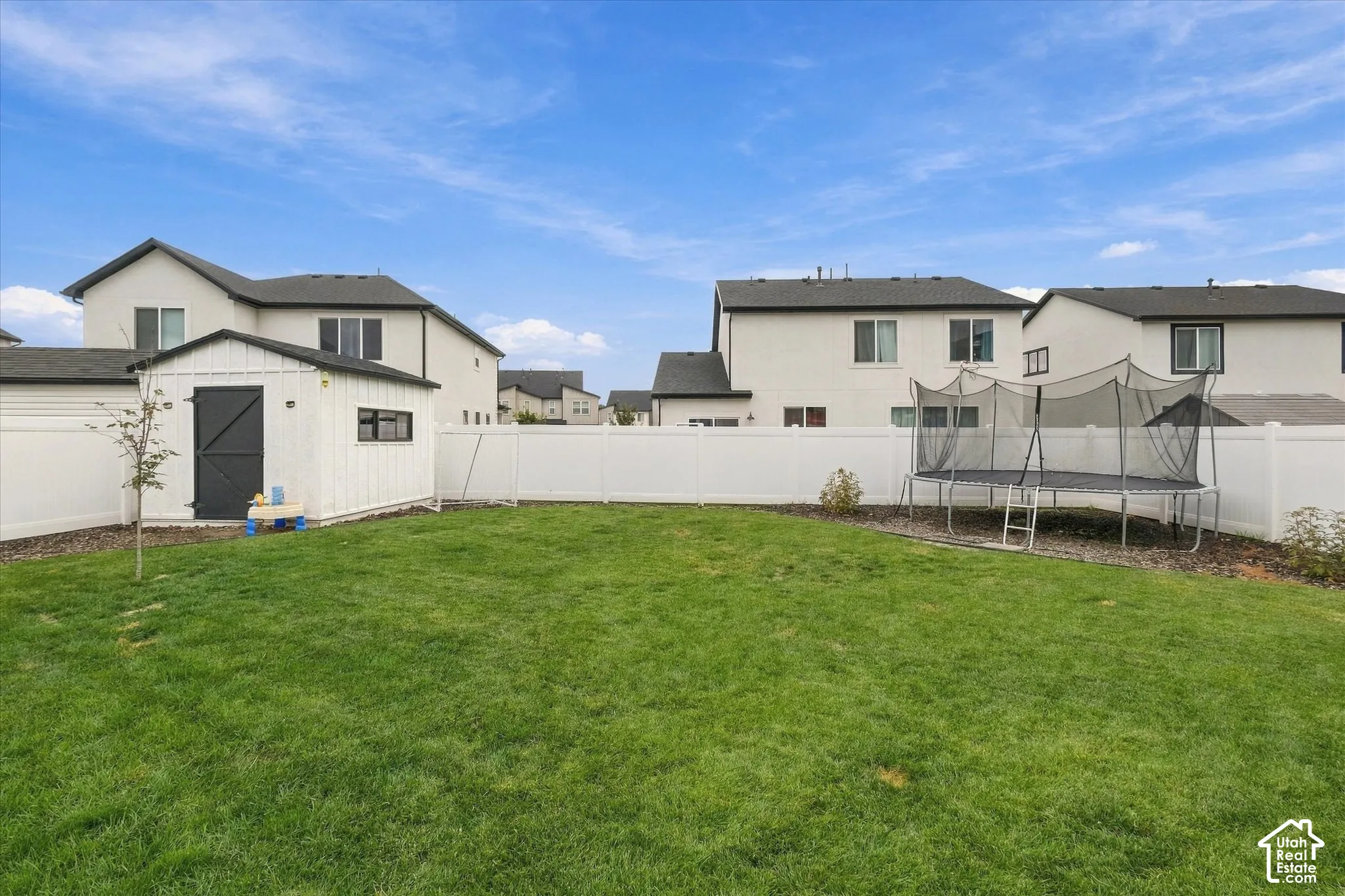 Expansive green lawn with a white privacy fence and a detached storage shed featuring a black barn door