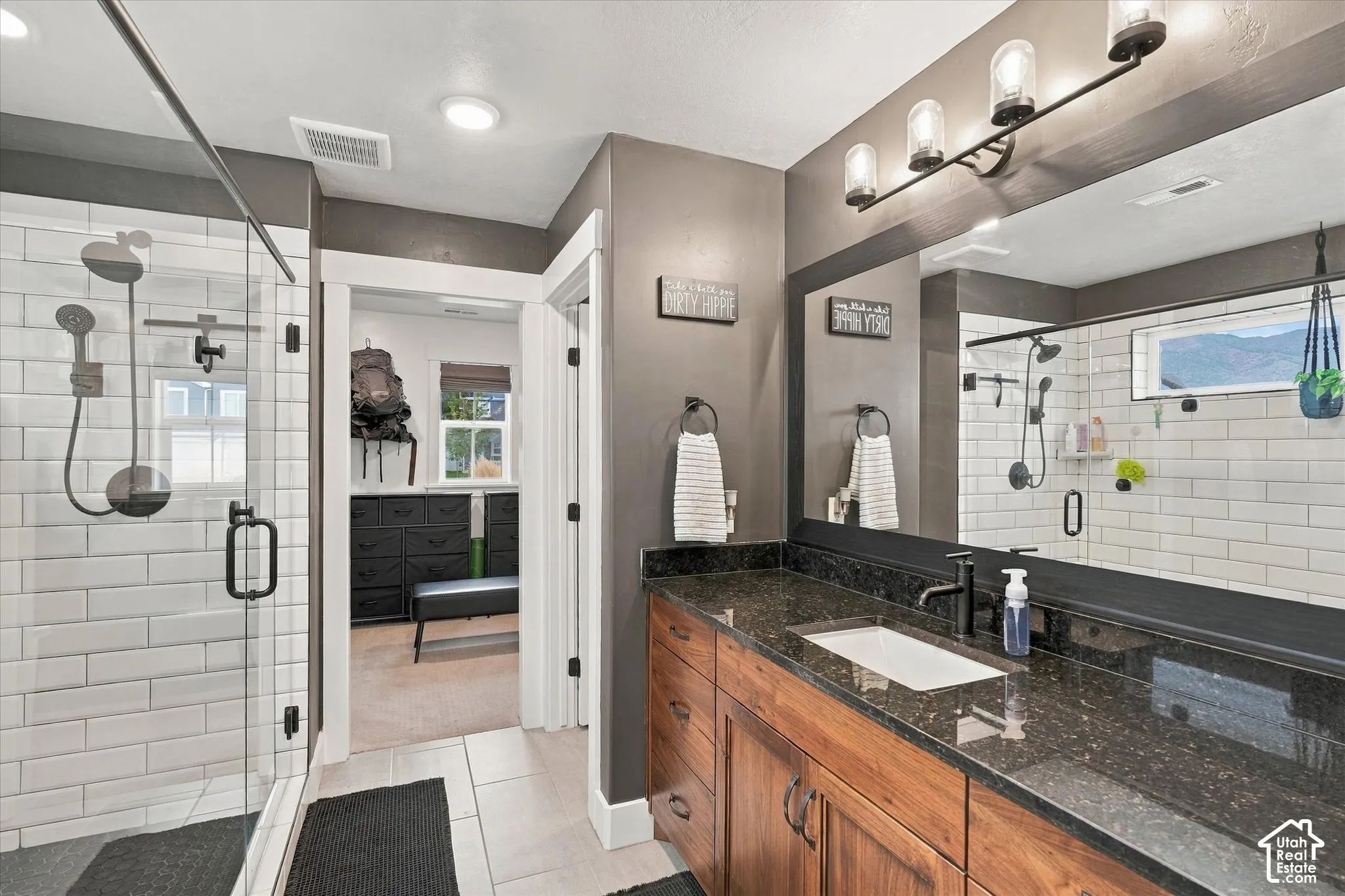 Walk-in shower with clear glass enclosure and subway tile surround, dark wood-finish vanity with an undermount sink, dark speckled countertop, and a large wall-mounted mirror