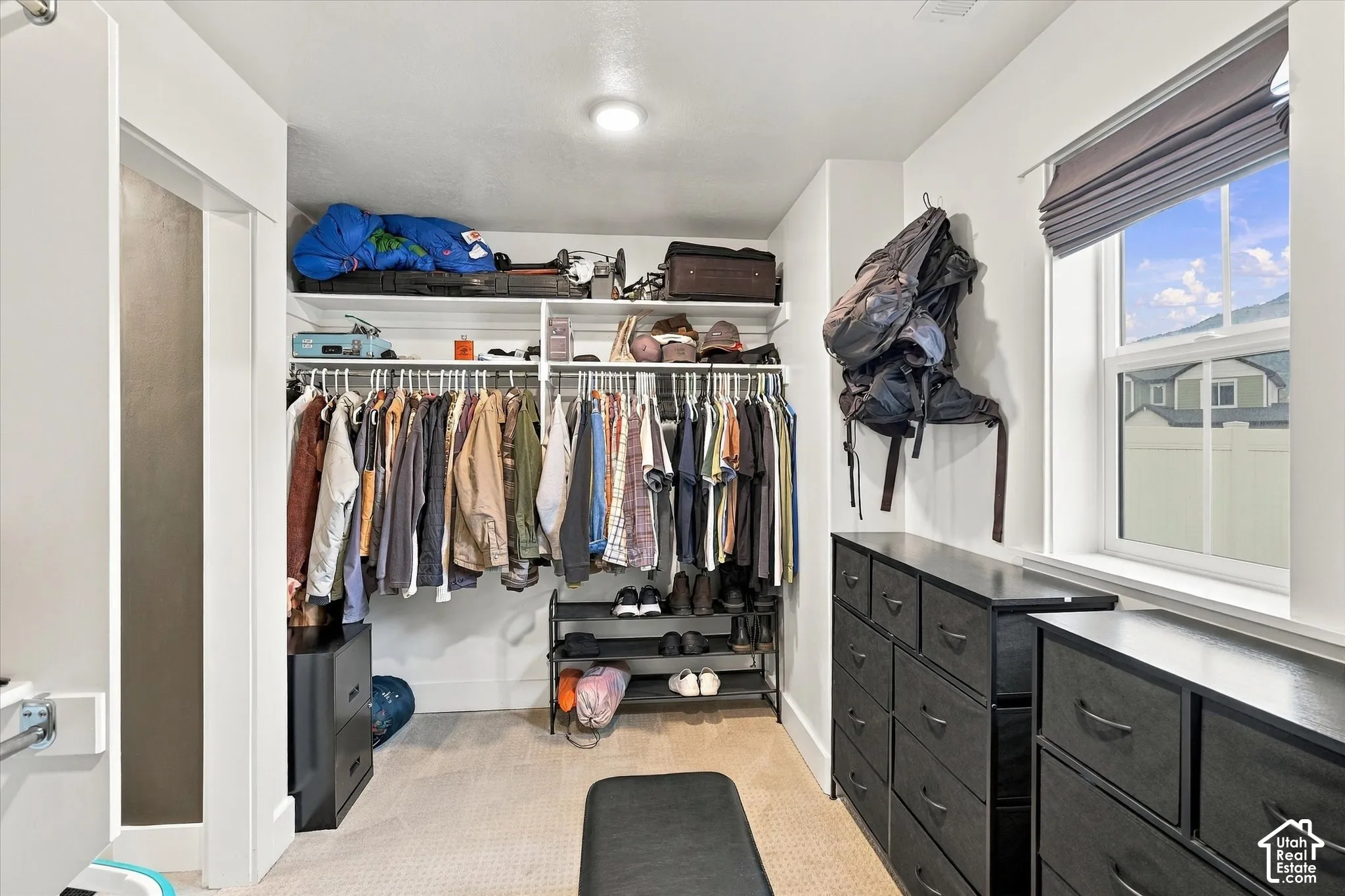 Recessed lighting illuminates the organized closet space featuring built-in shelving, hanging rods, and a window with a roller shade