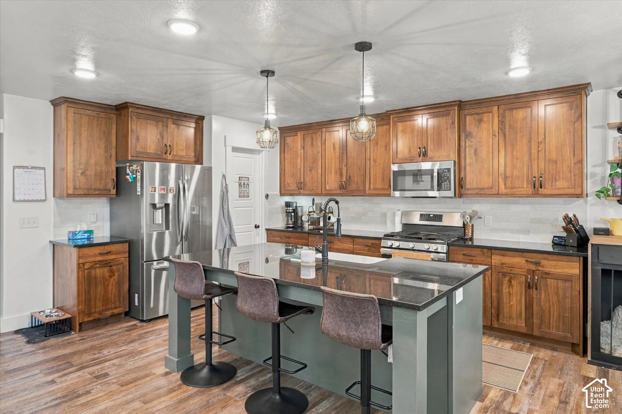 Kitchen featuring wood-finish flooring, dark stone countertops, wood cabinetry, a central island with seating, and stainless steel appliances