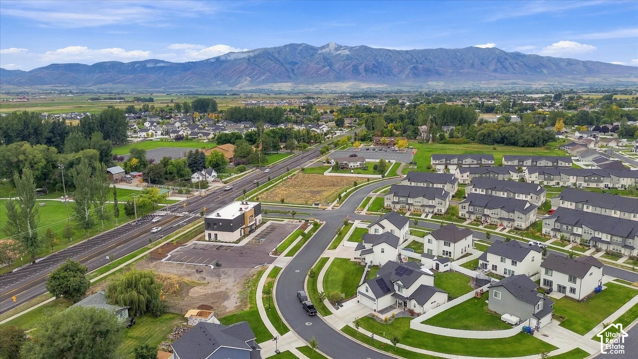 Mountain range backdrop, residential development with various home styles, curved street layout, manicured green spaces, and a commercial building