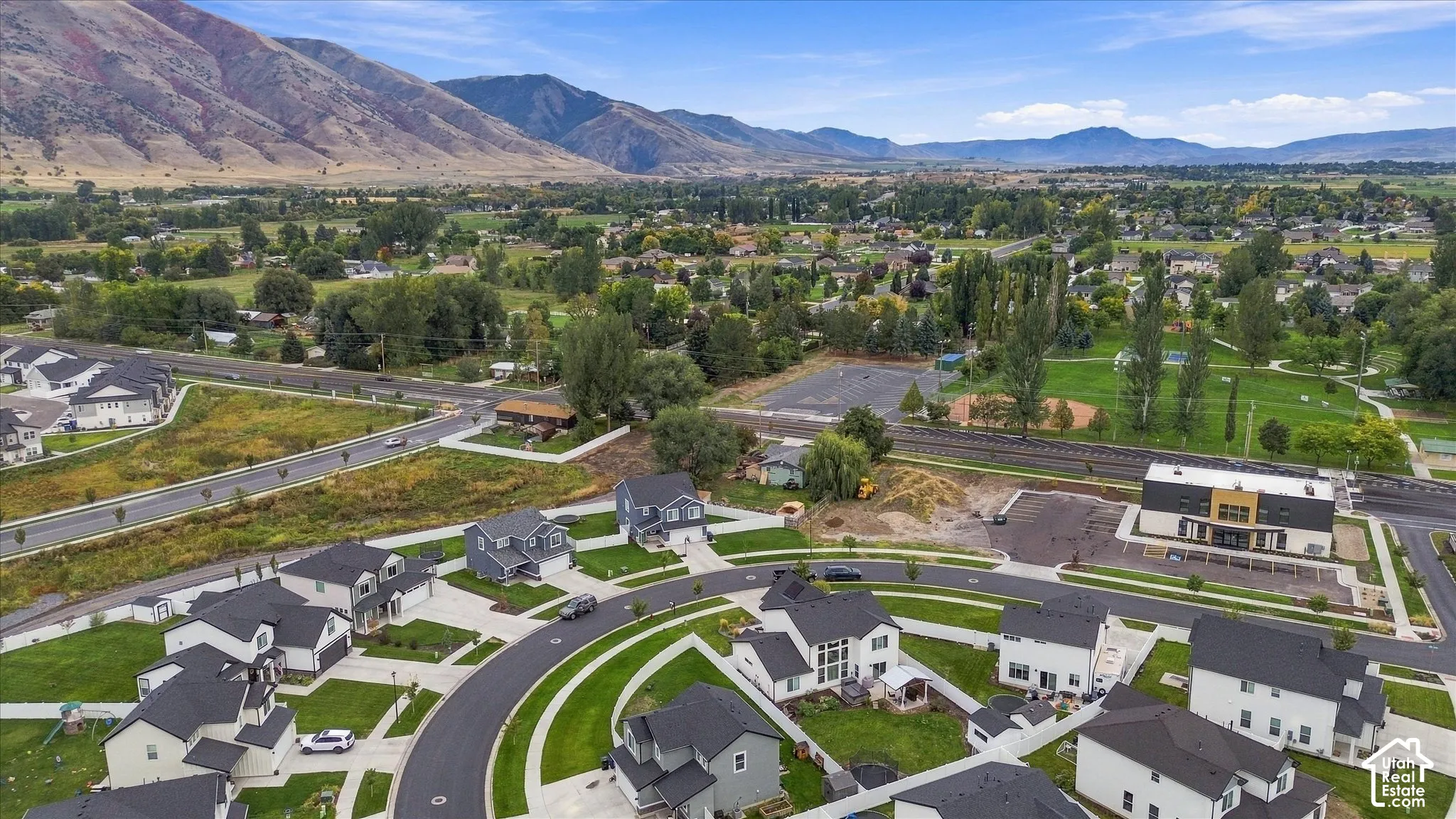 Modern residential development with a mountain backdrop, featuring a communal green space and paved roads