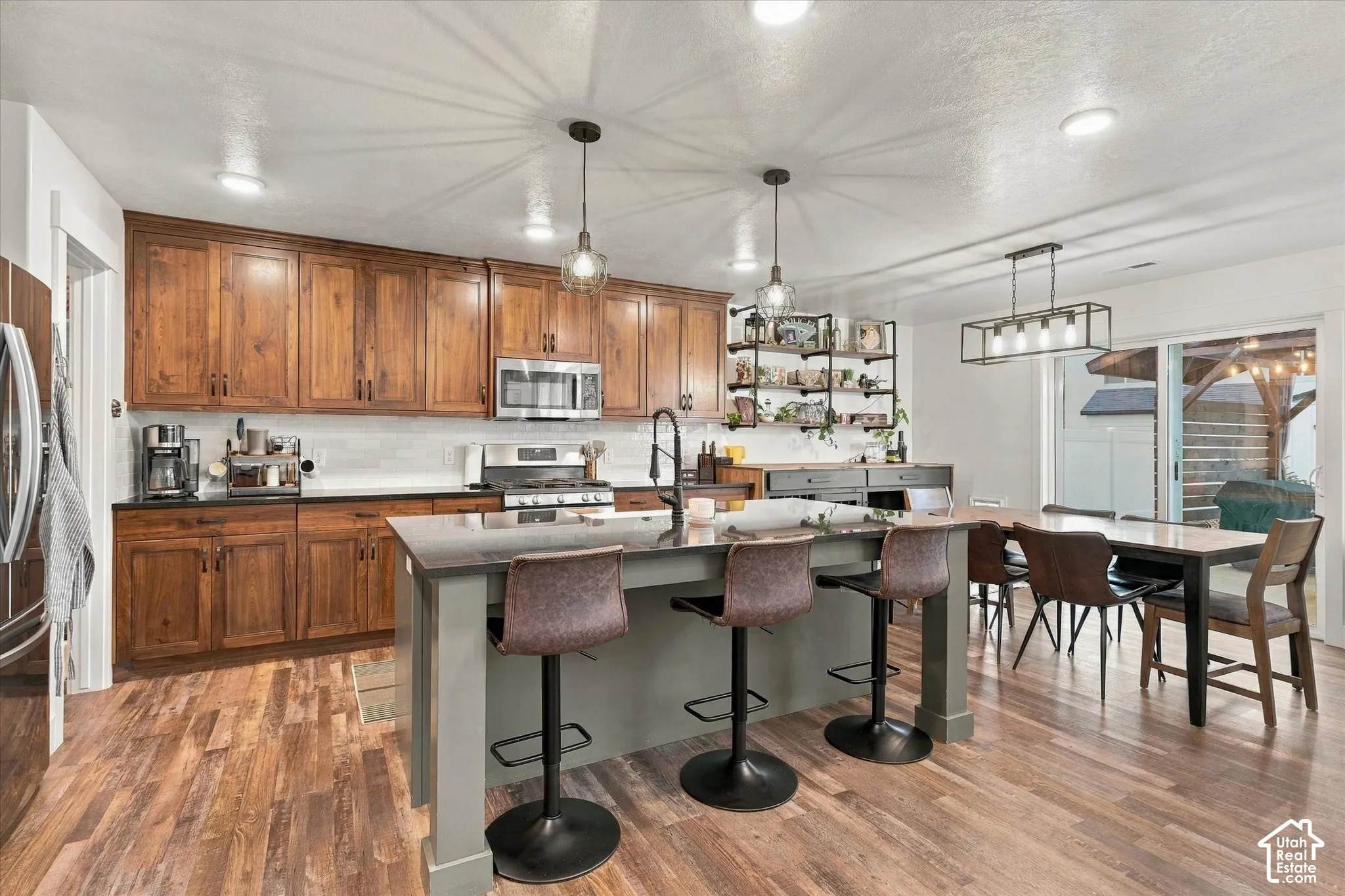 Wood-finish flooring throughout, kitchen island with seating, stainless steel appliances, wood cabinetry, and sliding glass door