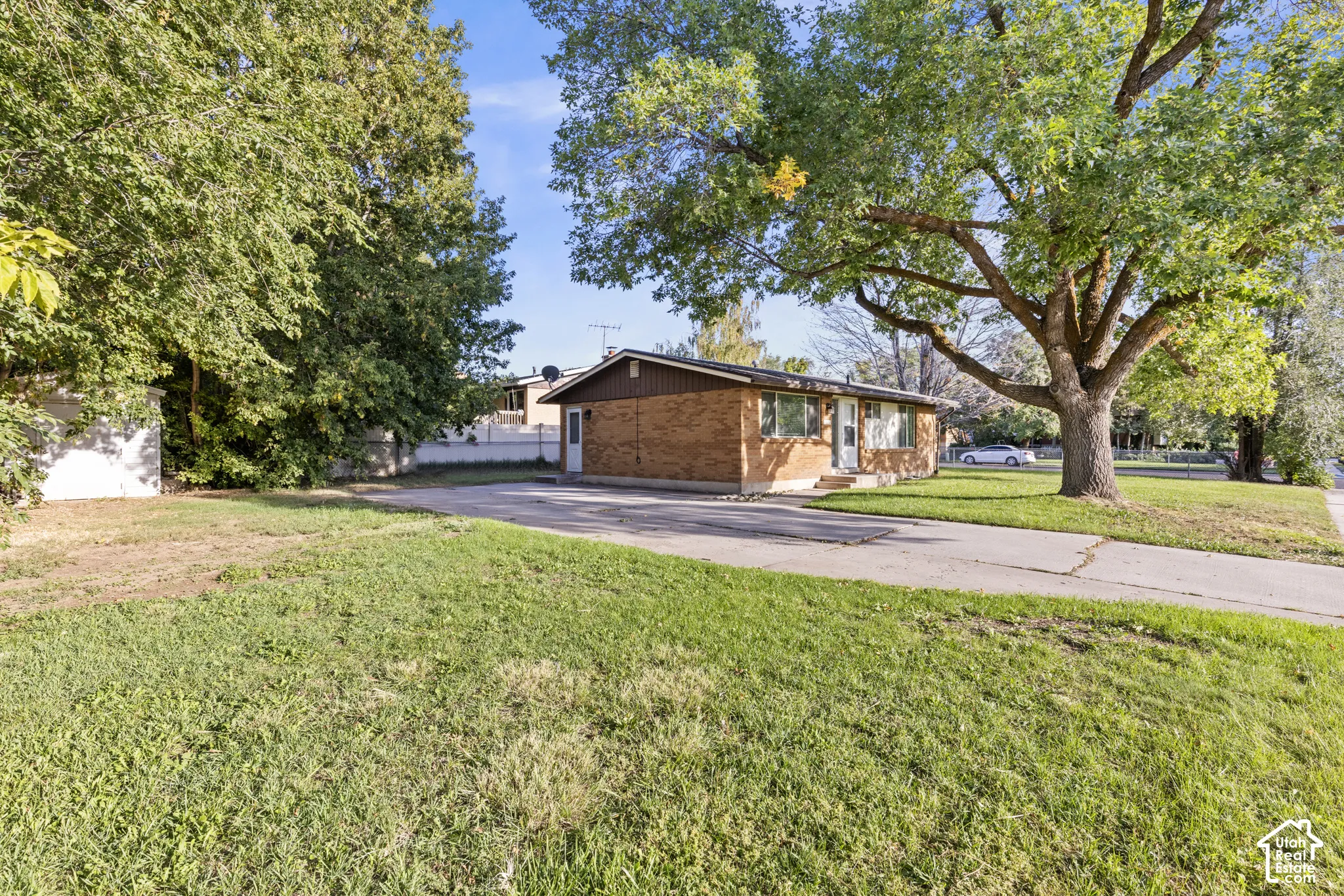 Brick exterior residence with a partial asphalt driveway, mature trees, and a grassy front yard
