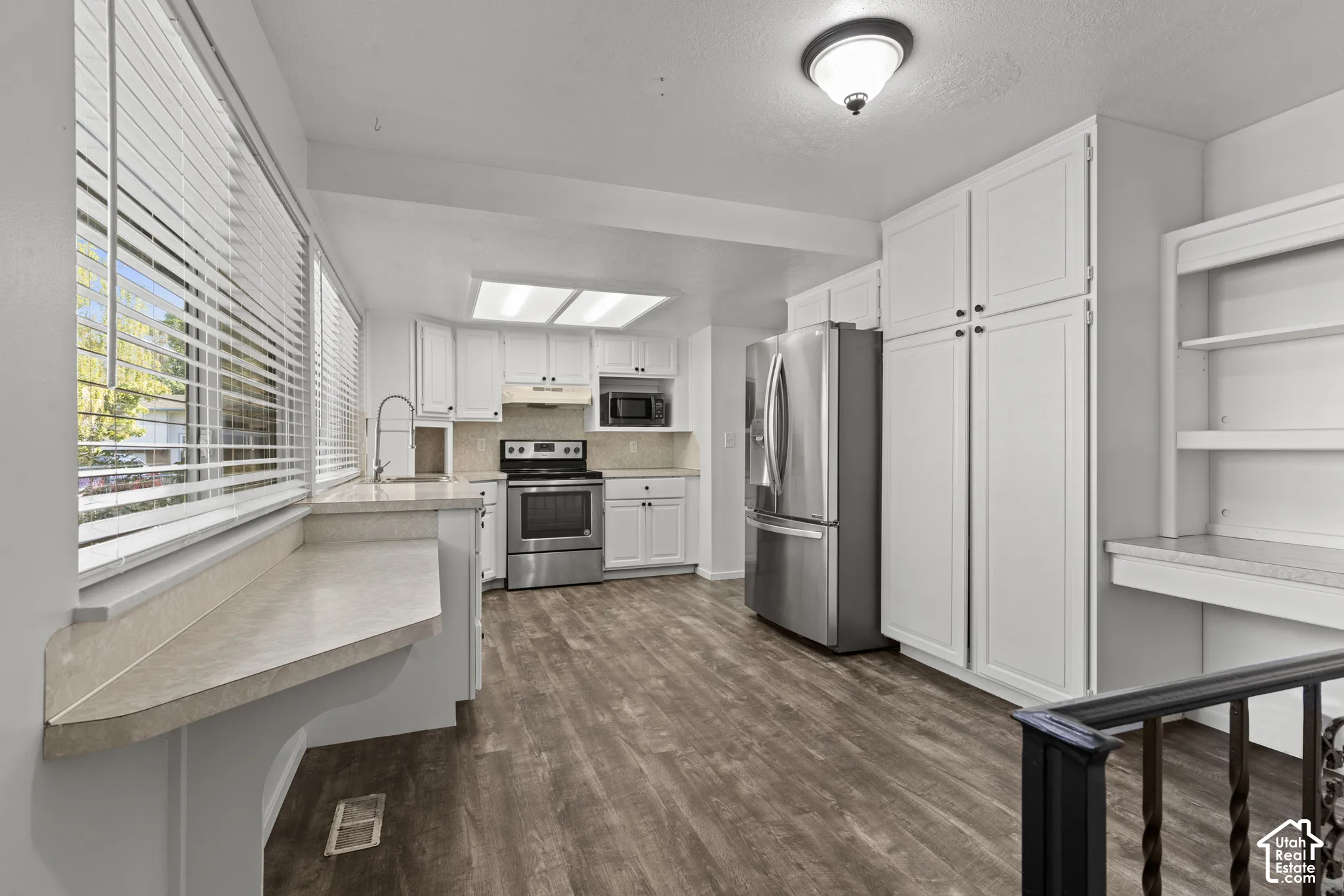 Full kitchen with stainless steel appliances, white cabinetry, wood-finish flooring, and a built-in desk area