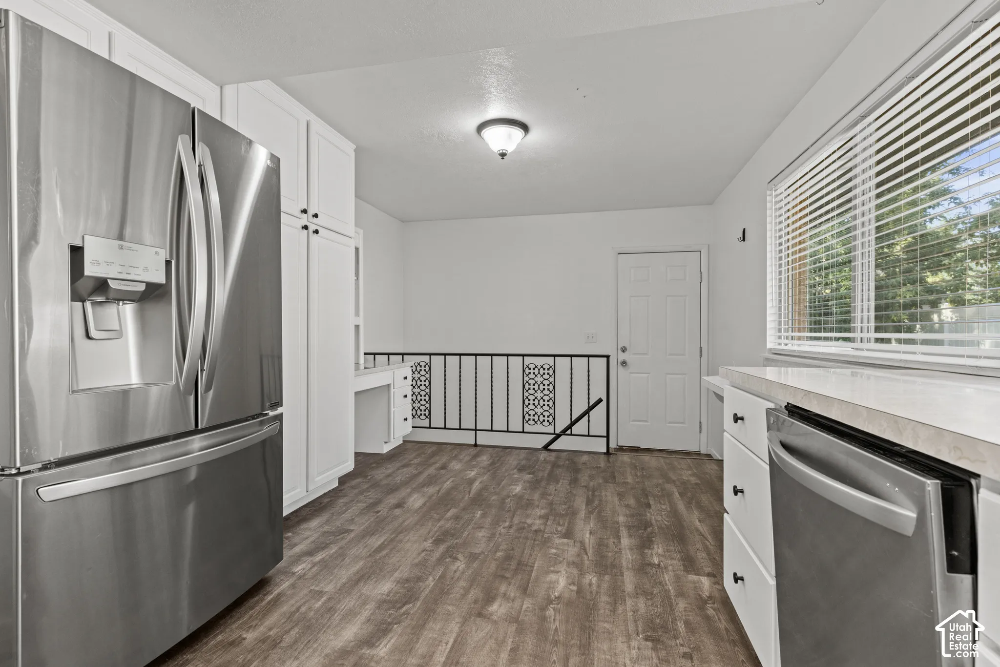Stainless steel French door refrigerator, white cabinetry, wood-finish flooring, built-in dishwasher, and a window with horizontal blinds