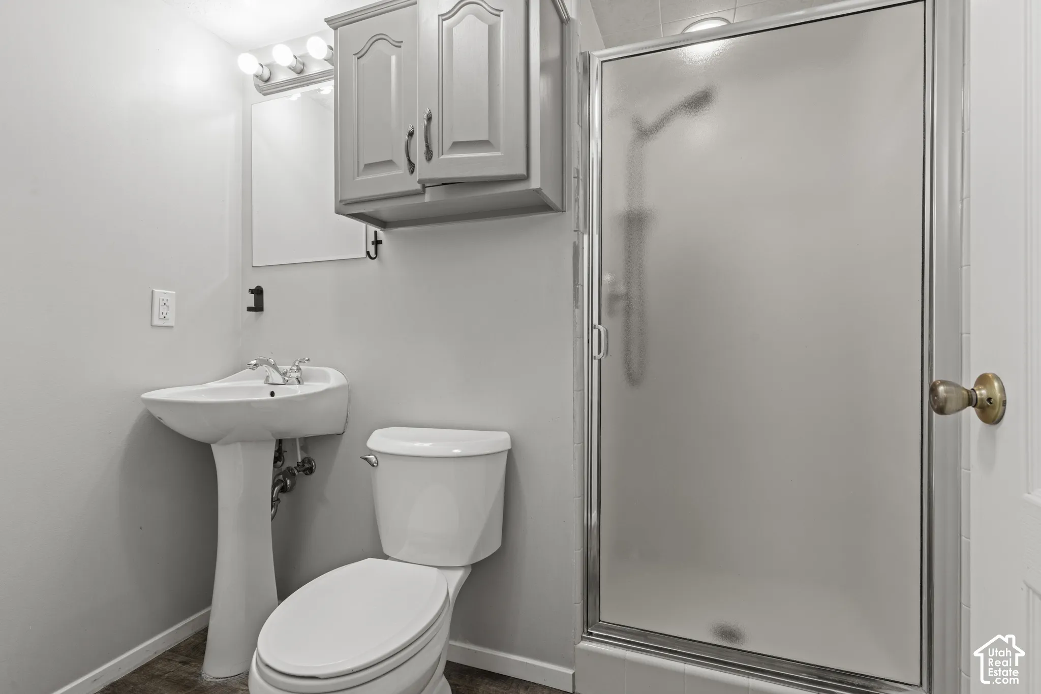 Pedestal sink with chrome fixtures, built-in medicine cabinet, and a shower with a frosted glass enclosure