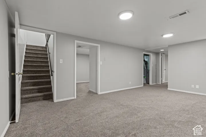 Carpeted flooring, light gray wall paint, white trim, recessed lighting, and a staircase with a black handrail