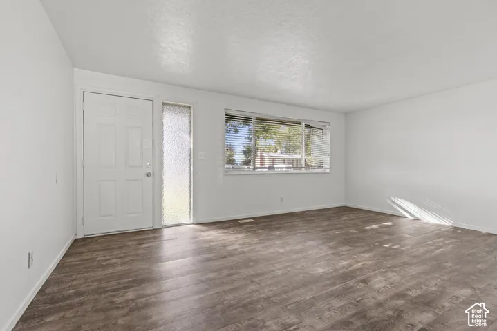 Six-panel entry door with sidelight, wood-finish flooring, and large window with blinds