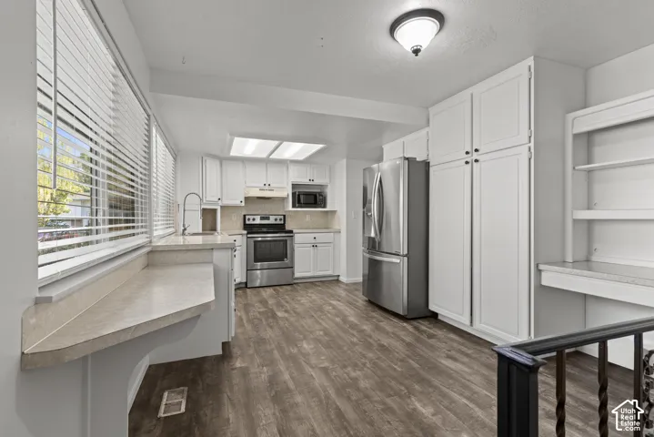 Full kitchen with stainless steel appliances, white cabinetry, wood-finish flooring, and a built-in desk area