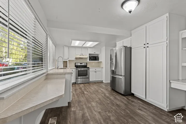 Kitchen featuring wood-finish flooring, white cabinetry, stainless steel appliances, and light-toned countertops