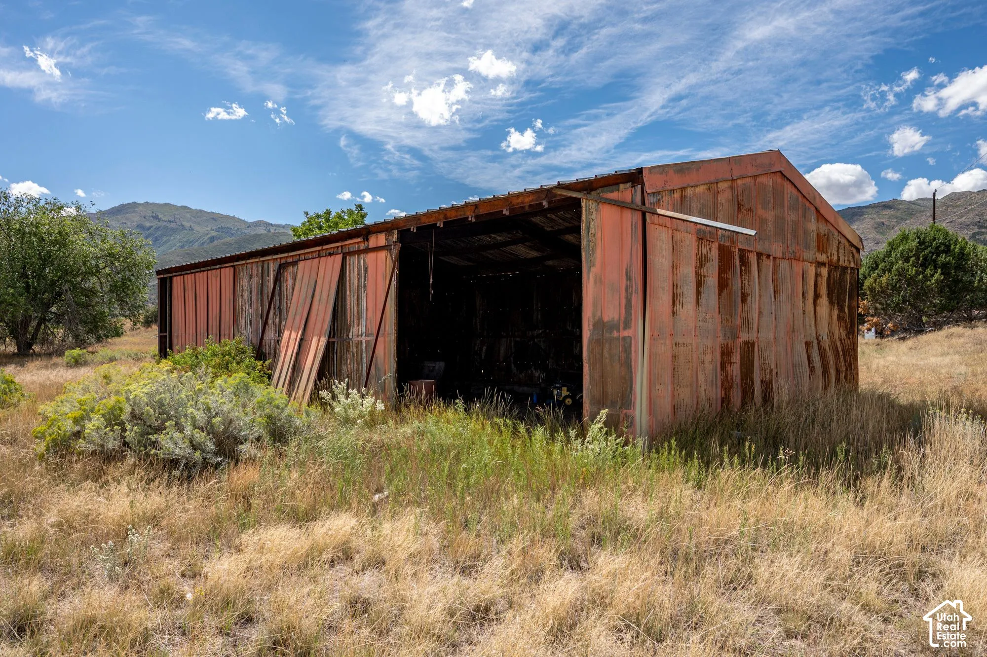 Corrugated metal barn with an open front and a metal roof, surrounded by natural landscaping