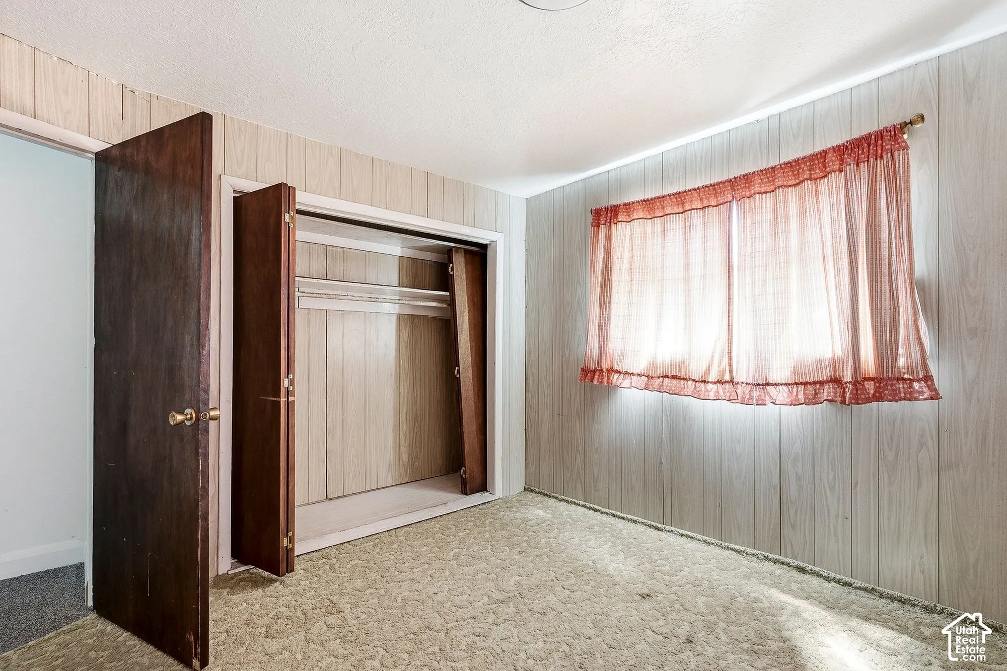 Light-toned wall paneling, wall-to-wall carpeting, and a built-in closet with bi-fold doors