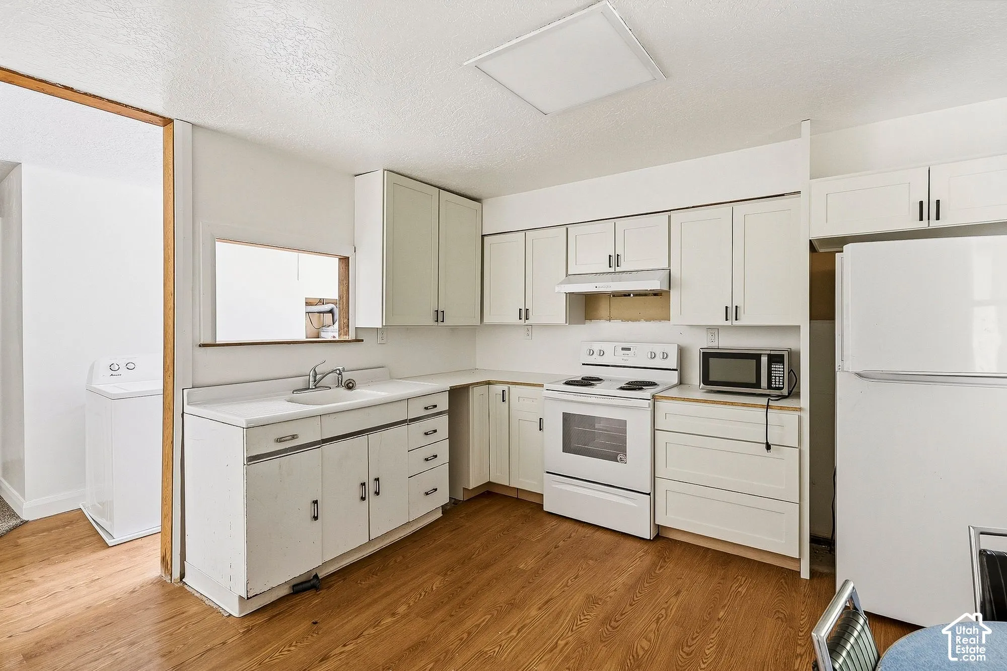 Kitchen featuring wood-finish flooring, white cabinetry with dark hardware, white countertops, a built-in range, and a pass-through window