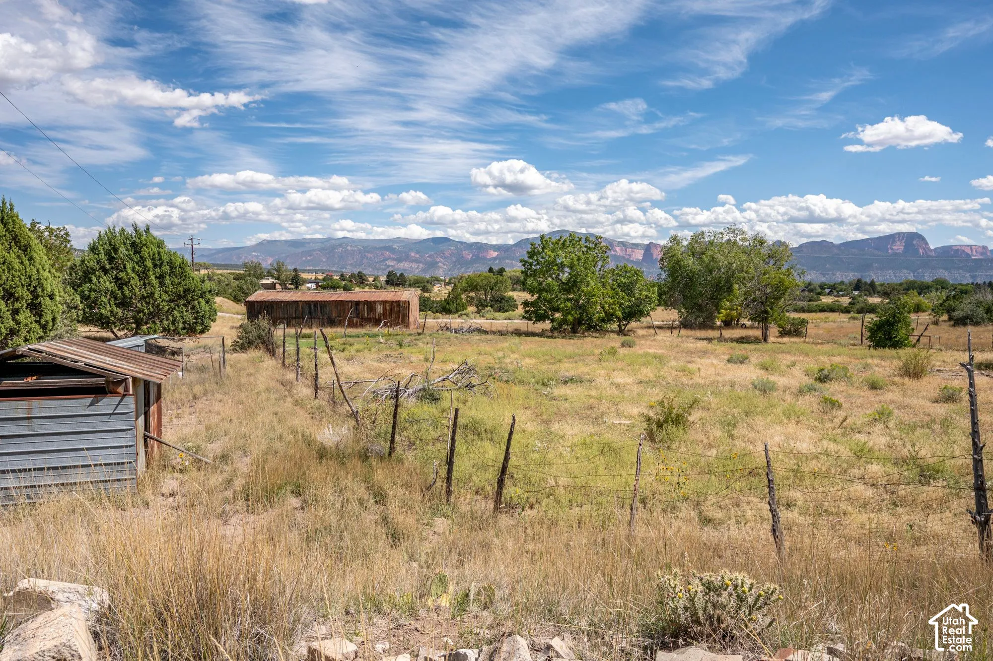 Expansive open land with distant mountain ranges, mature trees, and a weathered outbuilding