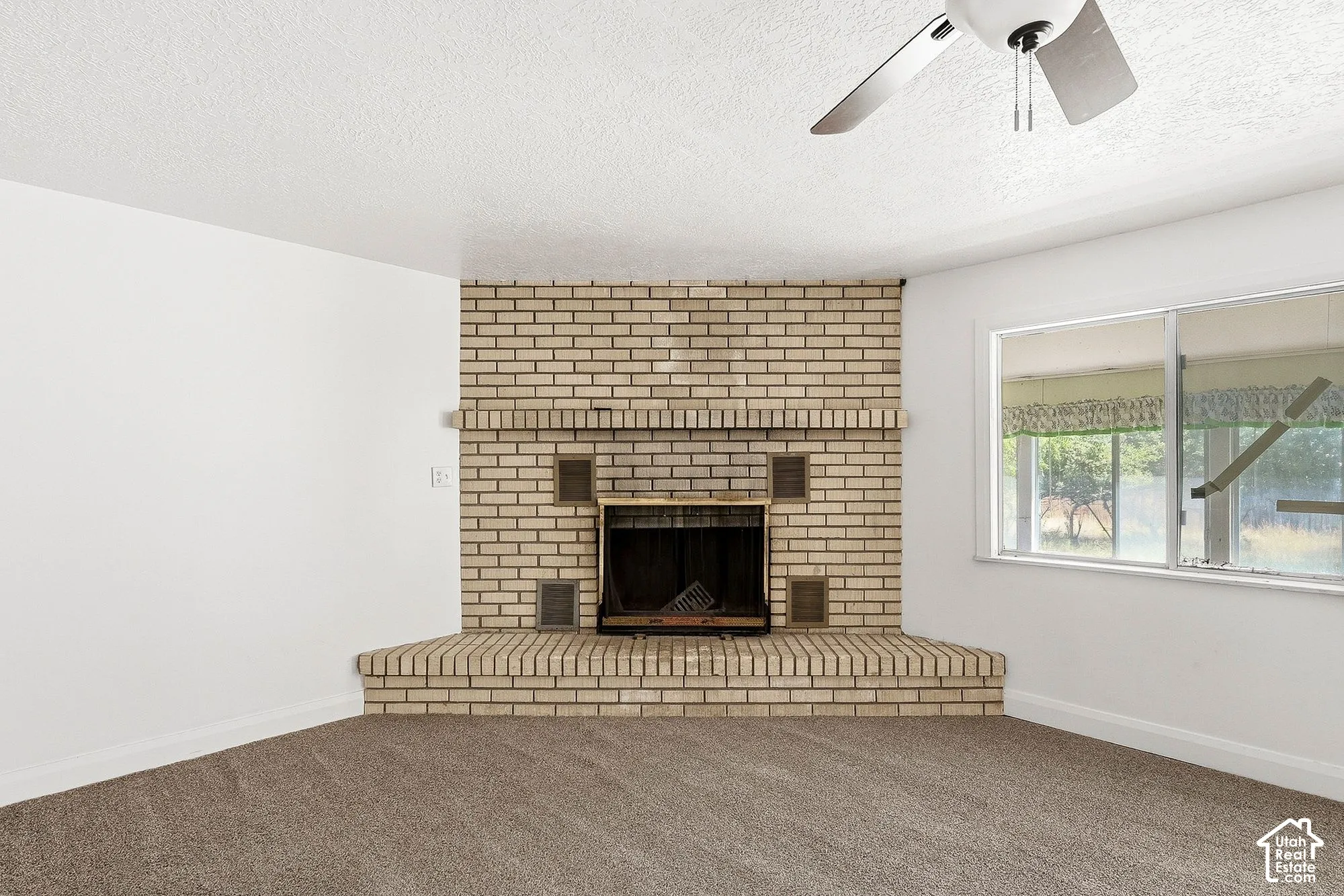 Brick fireplace with hearth, ceiling fan, and window