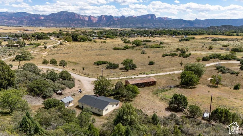 Expansive property featuring a single-story residence with a dark shingle roof, a detached shed, a secondary structure, and a dirt access road