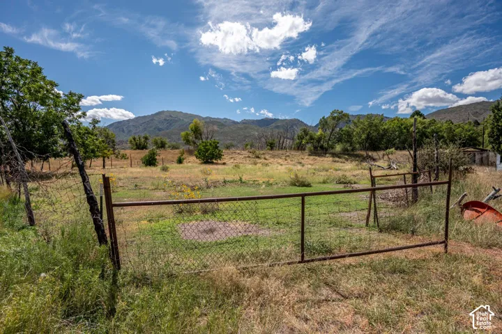 Fenced property with expansive terrain and mature trees, set against a backdrop of distant mountains
