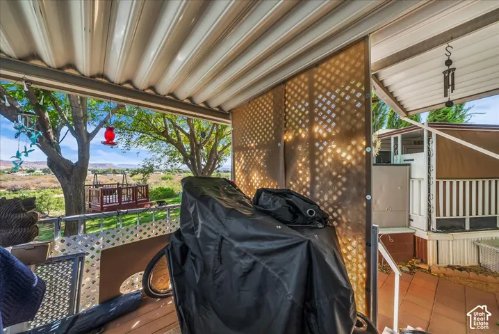 Covered patio with slatted ceiling, lattice privacy screen, and a distant elevated wood deck