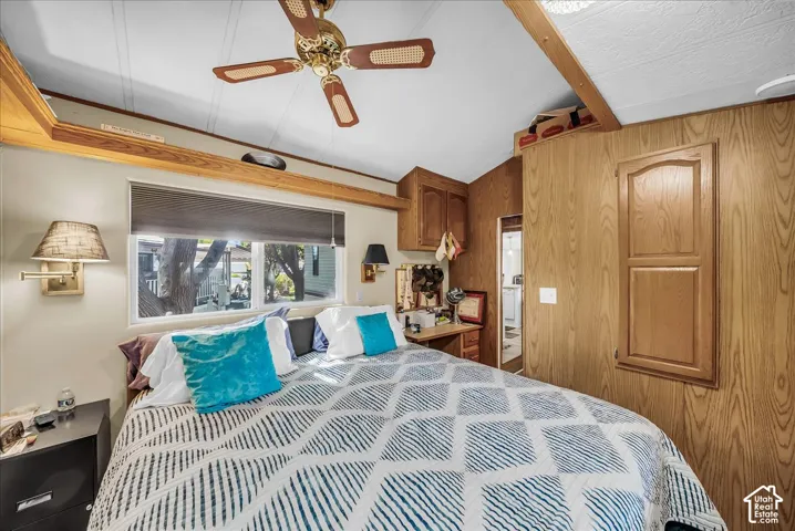 Vaulted ceiling with a ceiling fan, dual windows, wood-finish wall paneling, and built-in cabinetry
