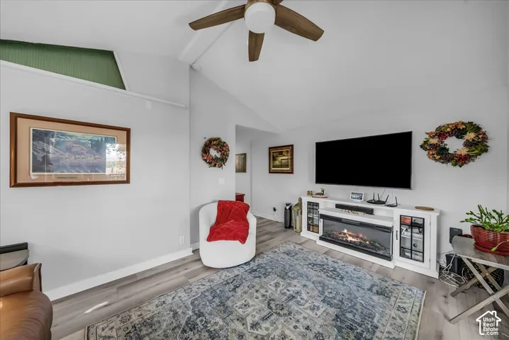 Vaulted ceilings with exposed beams, wood-finish flooring, and a built-in media console with an electric fireplace