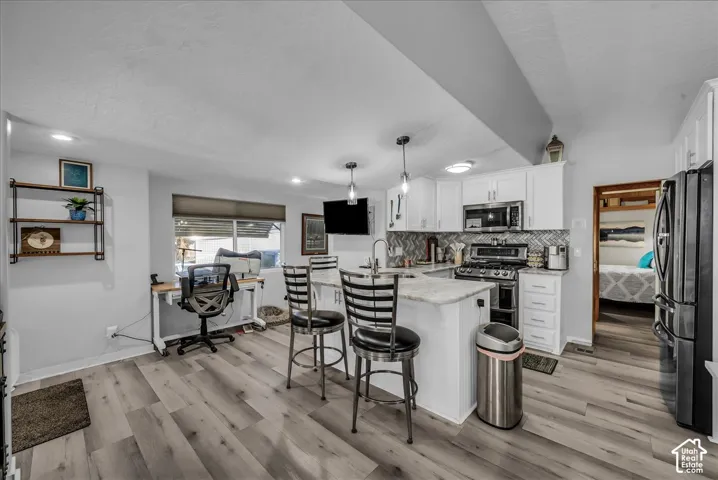 Open-concept kitchen with wood-finish flooring, white cabinetry, a herringbone tile backsplash, and a central island with bar seating