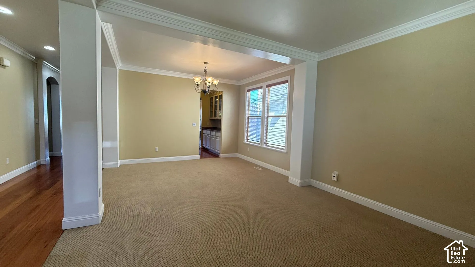 Open concept living space with carpeted flooring, crown molding, and a chandelier light fixture