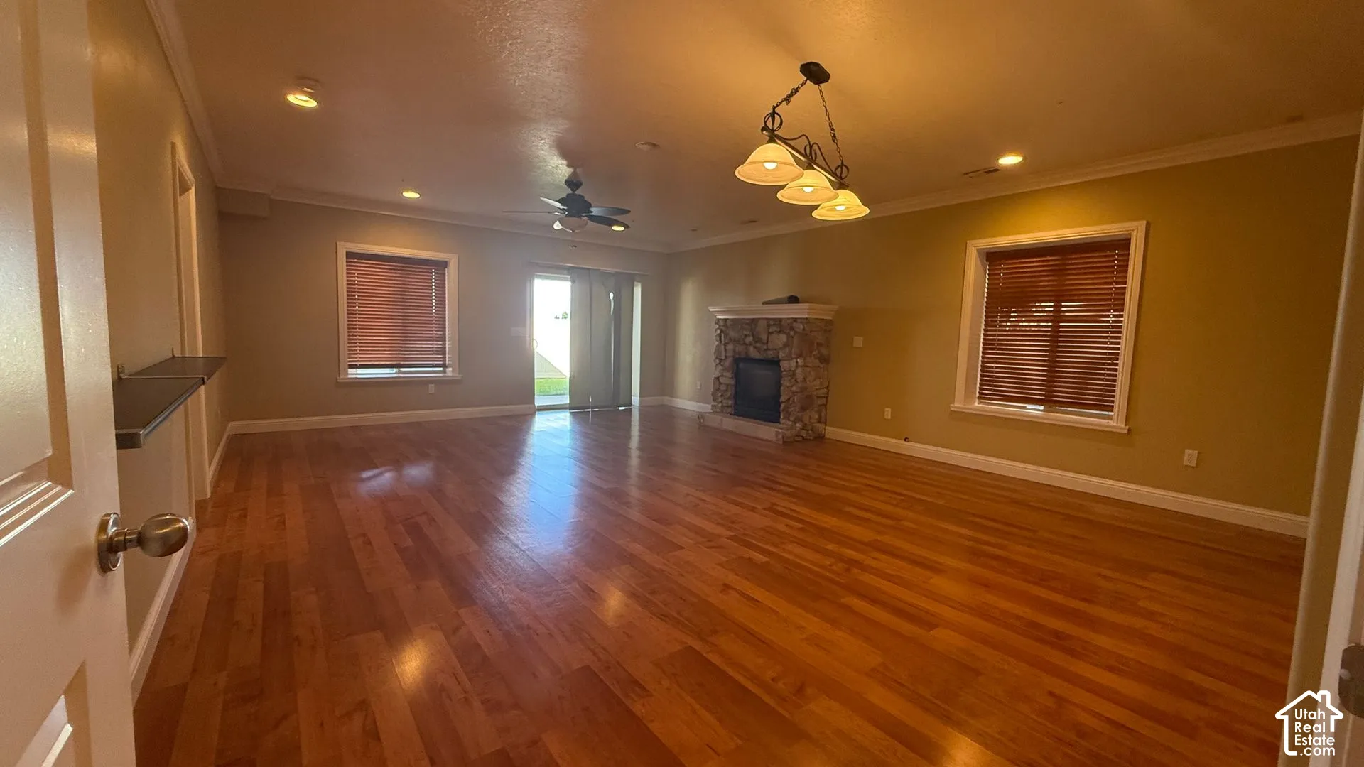 Spacious room featuring wood-finish flooring, a stone-clad fireplace, and sliding glass door