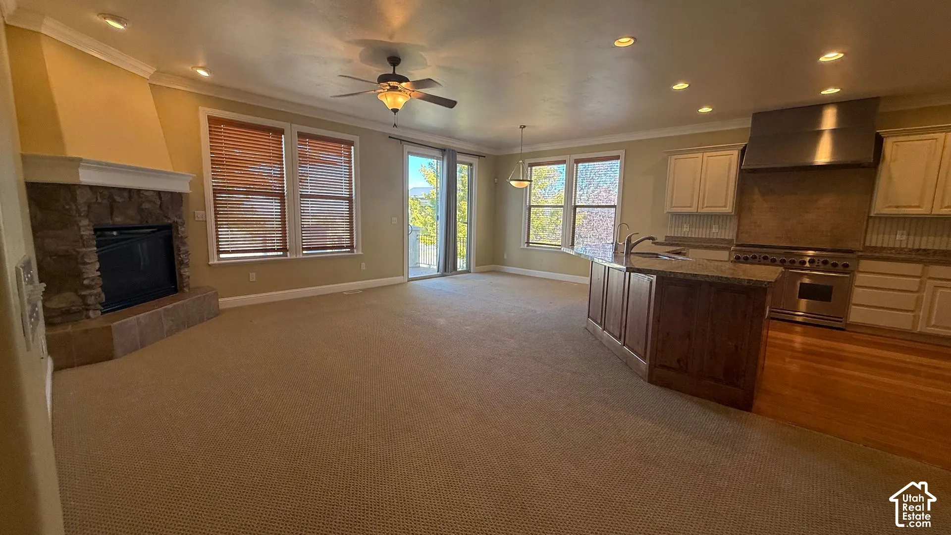 Open-concept living area featuring a stone fireplace, carpeted flooring, and a ceiling fan