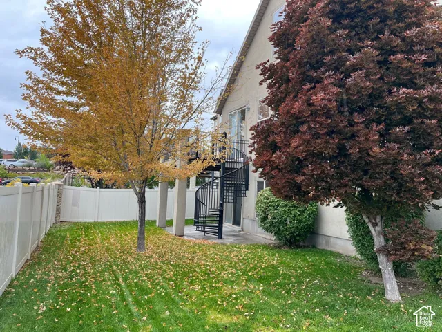 Spiral exterior staircase, landscaped yard, privacy fencing, mature trees, and stucco exterior
