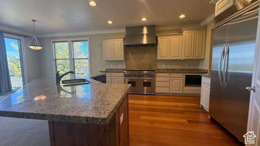 Gourmet kitchen featuring a large island with sink, stainless steel appliances, light-toned cabinetry, and wood-finish flooring