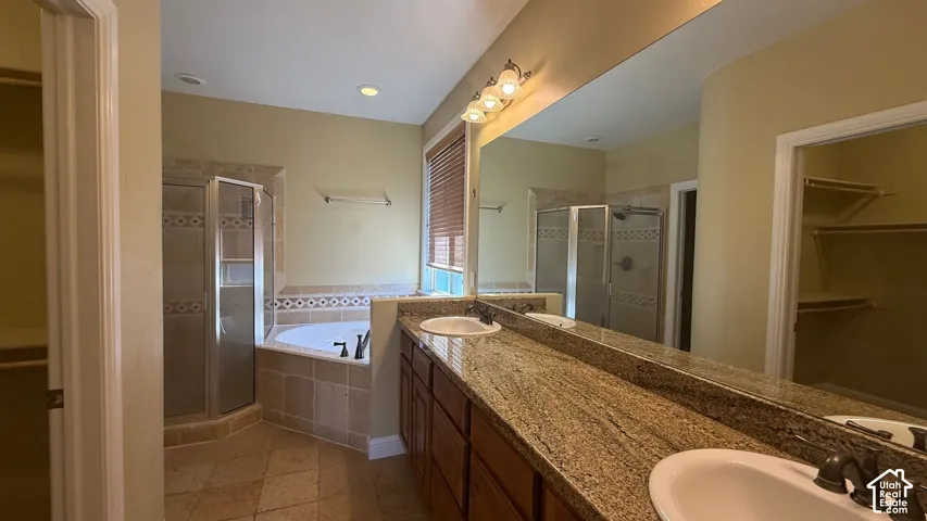 Dual vanity with granite countertop, integrated soaking tub, tiled shower enclosure with glass door, and recessed lighting