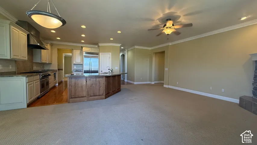 Expansive open concept interior featuring a kitchen island, wood-finish flooring, recessed lighting, crown molding, and a built-in stone fireplace