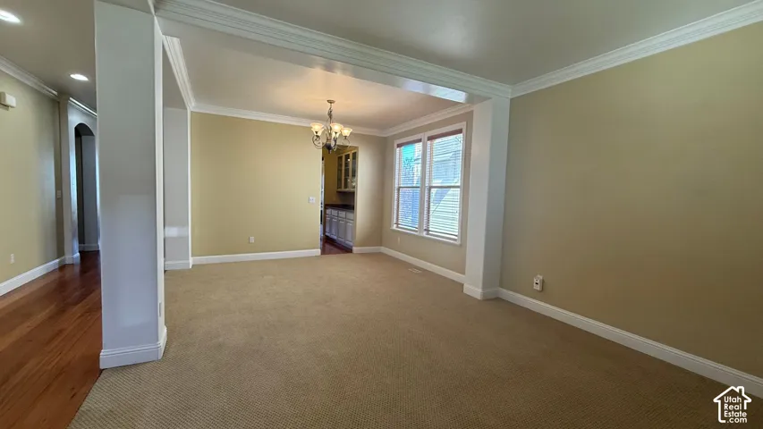 Open concept living space with carpeted flooring, crown molding, and a chandelier light fixture