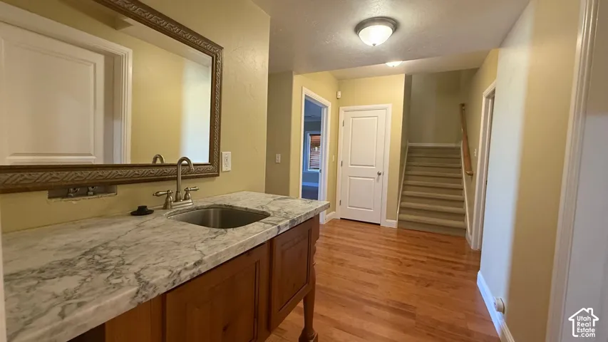 Wood-finish flooring, built-in vanity with integrated sink, stone-finish countertop, decorative framed mirror, and carpeted staircase