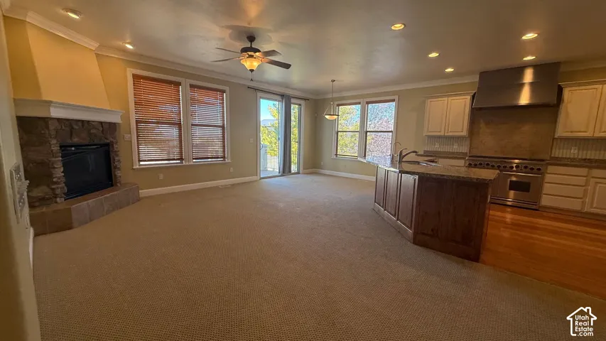 Open-concept living area featuring a stone fireplace, carpeted flooring, and a ceiling fan