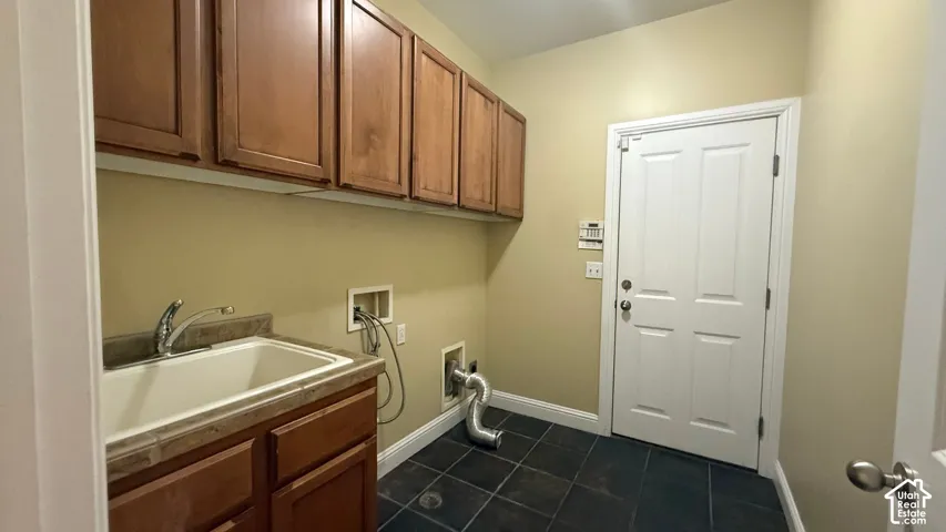 Utility room featuring upper cabinetry, a counter with an integrated sink, a faucet, and dark tile flooring