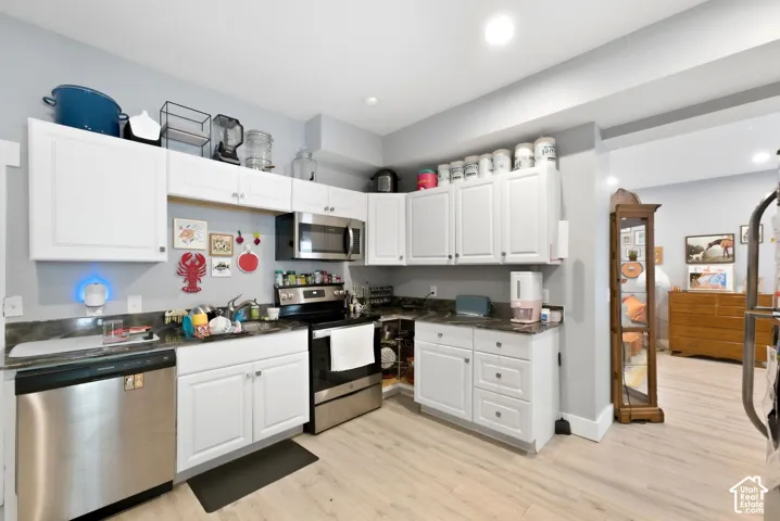 White shaker-style cabinetry with stainless steel appliances, dark countertops, and wood-finish flooring