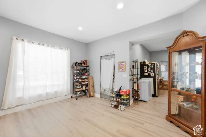 Light wood-finish flooring, recessed ceiling lighting, a large window with blinds, and an open doorway