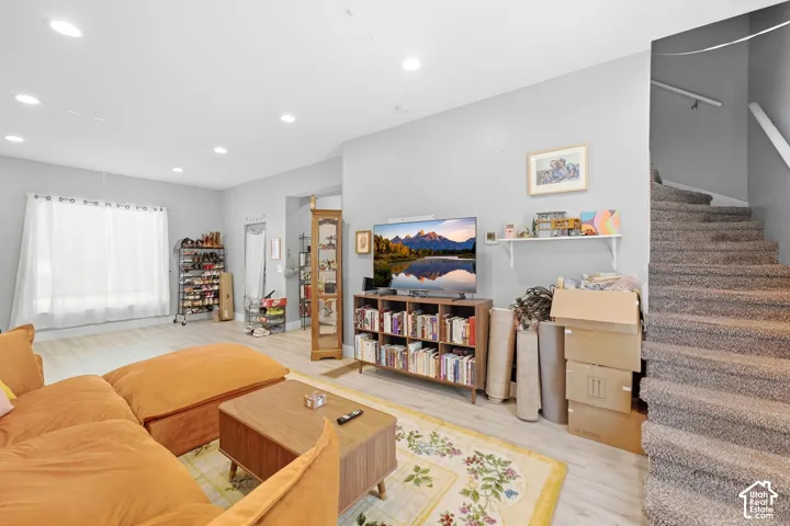 Recessed lighting, light-toned wood-finish flooring, and a carpeted staircase with a white handrail