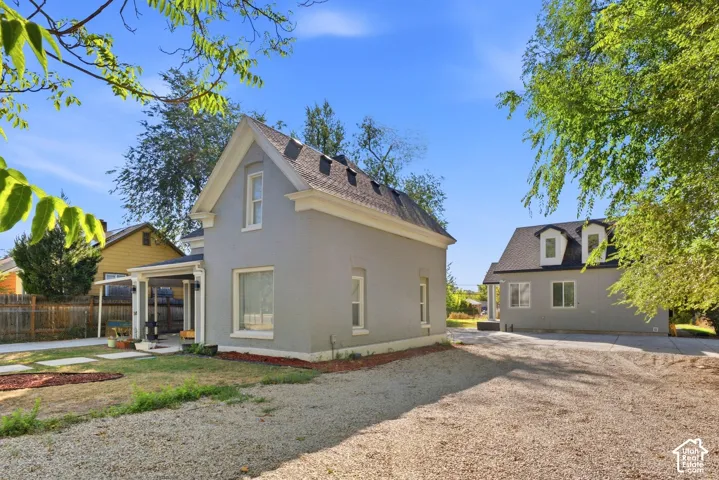 Two-story gray stucco residence with white trim, featuring an attached covered porch and a gabled roof. Front side of triplex.