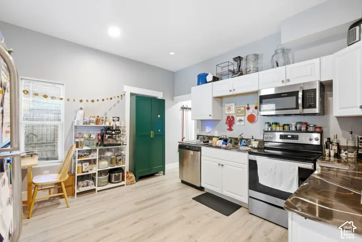 Modern kitchen featuring stainless steel appliances, white cabinetry, a built-in microwave, wood-finish flooring, and a large window