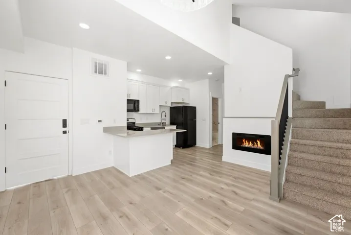 Open-concept living area with wood-finish flooring, a contemporary built-in fireplace, and a carpeted staircase with a wood handrail