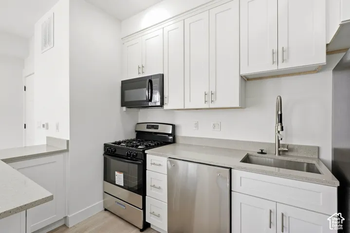 White shaker-style cabinetry, light-toned countertops, stainless steel appliances, and a stainless steel sink with a high-arc faucet