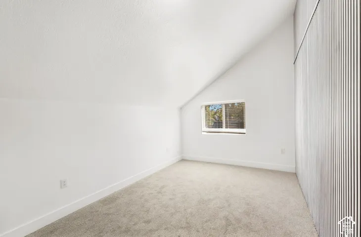 Sloped ceiling room featuring carpet flooring, crisp white walls, and a recessed window with blinds