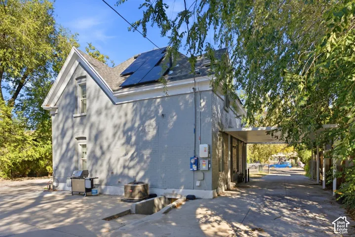 Gray brick exterior with white trim, featuring solar panels on the roof and a covered carport leading to a paved driveway. Back of main house.