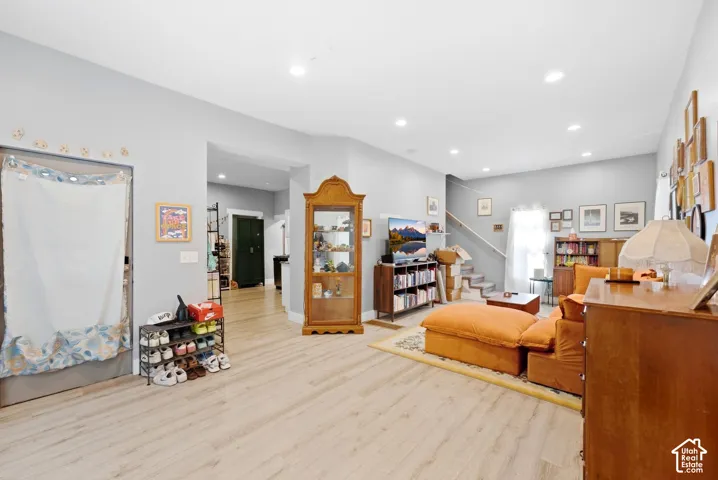 Spacious living area featuring light wood-finish flooring, recessed lighting, and a staircase with a wood handrail