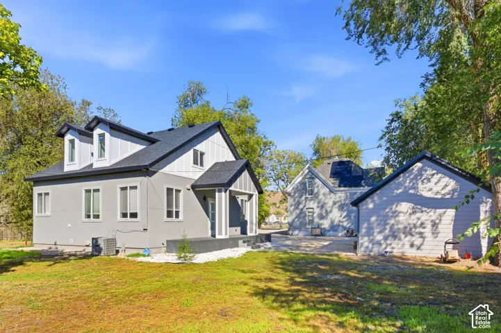 Contemporary exterior with dormer windows, dark roof, light gray siding, and a covered entry. Back side of triplex.